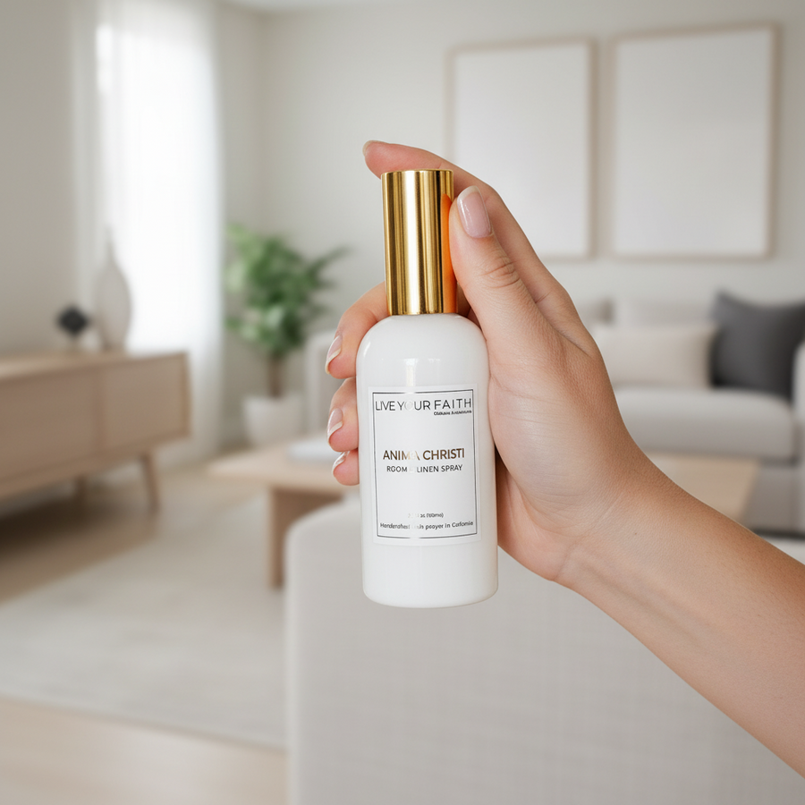 Hand holding our catholic Anima Christi in rose water scent room spray bottle with gold cap in a blurred indoor .setting