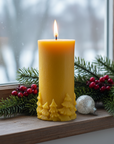 A yellow beeswax candle with an intricate pine tree detail along the bottom edge.