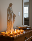 Statue of Virgin Mary with candles and an open bible on a wooden surface.