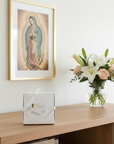 Framed religious artwork above a wooden console table with a vase of flowers and a gift box.