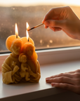 Person lighting a candle shaped like the Holy Family with a match by a window.