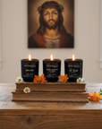 Three lit candles on books with a religious painting in the background