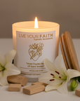 Candle with 'Live Your Faith' packaging surrounded by white lilies on a neutral background