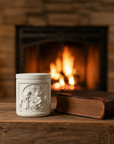 White embossed candle jar on a wooden surface with a fireplace in the background