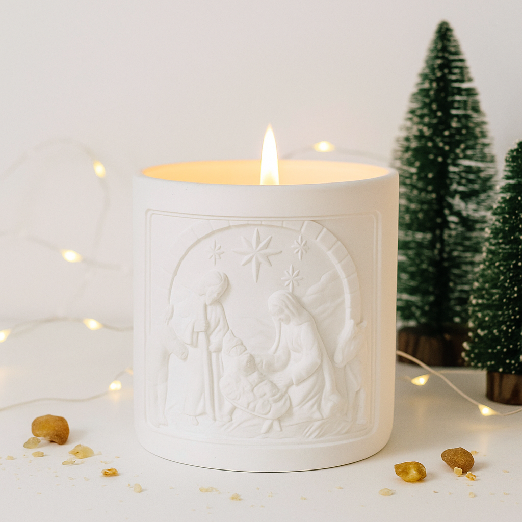 White candle with nativity scene design in a decorative setting with small trees and lights.