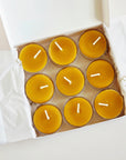 Nine yellow  beeswax candles in a cardboard box on a white background