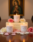 Candles with 'Live Your Faith' packaging on a table with flowers, blurred religious painting in the background. Three candles inspired by Virgin Mary