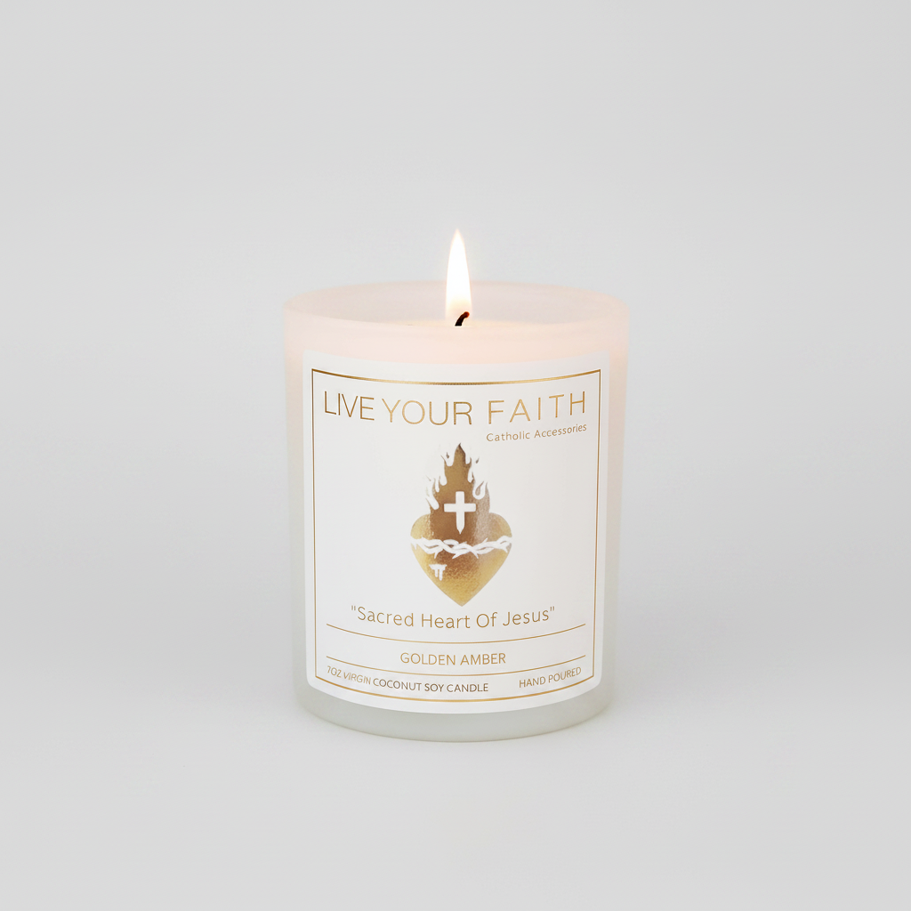 The "Sacred Heart of Jesus'" 7oz scented prayer candle by Live Your Faith Catholic. It is a lit, white matte glass jar with a white paper label and a gold-stamped Sacred Heart graphic, centered against a seamless warm grey studio background.