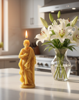 Candle shaped like Saint Joseph next to a vase with white lilies on a kitchen counter.
