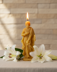 Beeswax Candle shaped like Saint Joseph with two white lilies on a textured surface