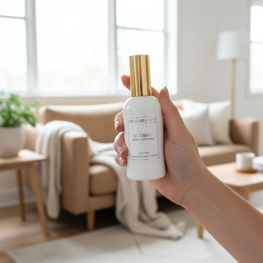 Hand holding our Saint Joseph a room spray bottle in a bright living room.