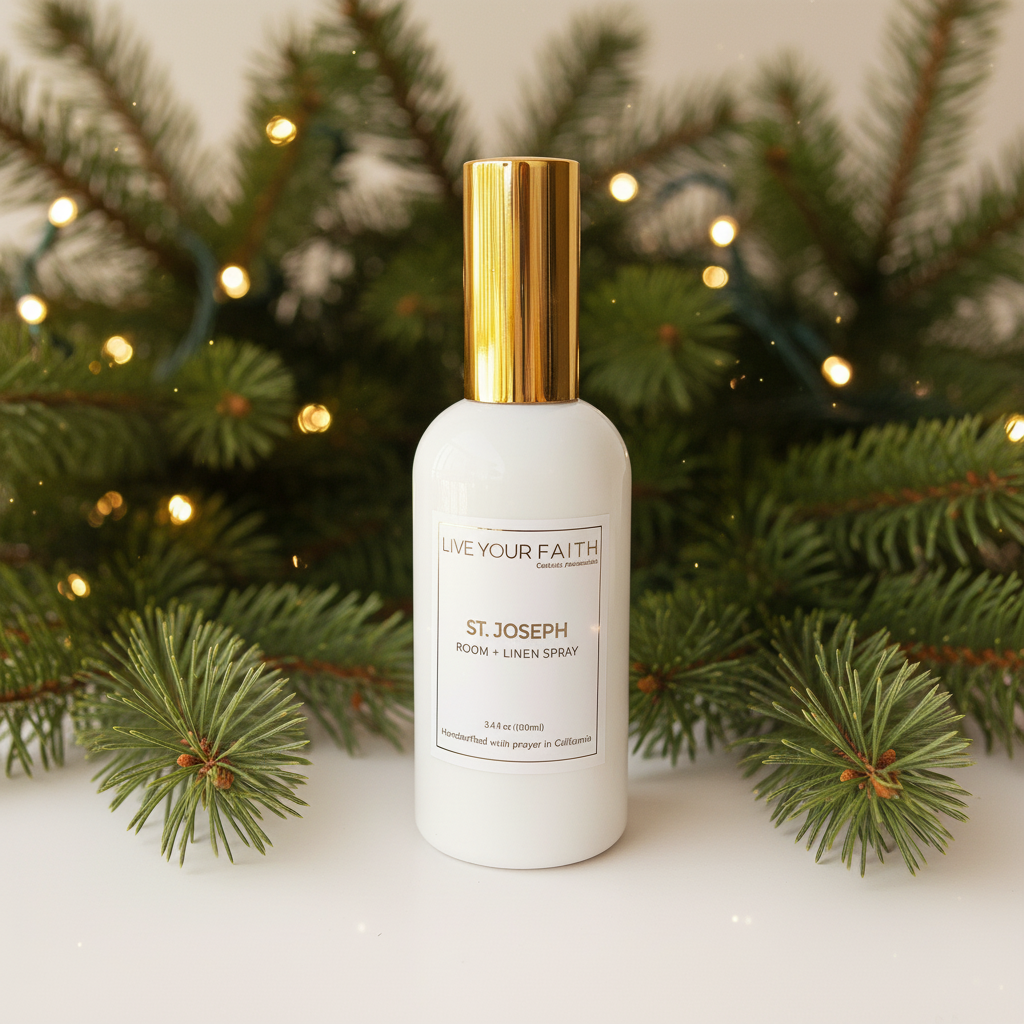 White Saint Joseph room spray bottle with gold cap on a white surface with Christmas tree branches and lights in the background