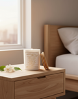 Candle with the serenity prayer on a wooden nightstand next to a bed with pillows