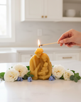 Hand lighting a candle shaped like the holy family with flowers on a kitchen counter.